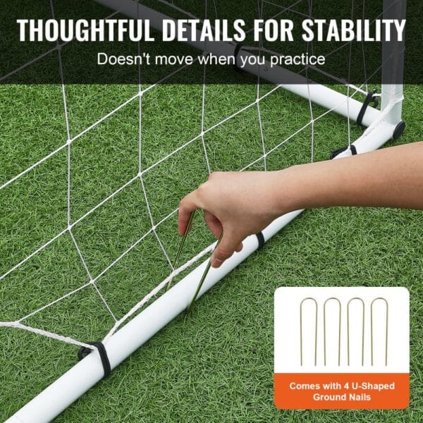 hand securing VEVOR soccer rebound trainer net to ground with u-shaped nails for stability on grass.